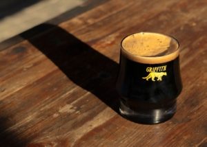 A close-up of beer in a glass with 'Griffith' and a yellow P-22 icon, placed on a sunlit wooden table