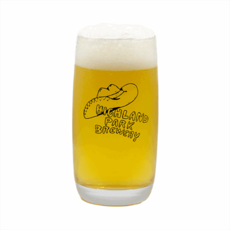 A pint glass filled with a hazy, pale yellow beer topped with a thick, foamy head. The glass has "Highland Park Brewery" and a cowboy hat logo printed on it.