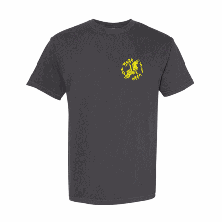 The Timbo Week 2025 Tee is a plain black short-sleeve t-shirt featuring a small yellow circular graphic and the text "THIS MUST BE THE WEEK" around a stylized hand pointing upward on the left chest.