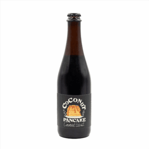 A dark glass beer bottle with a label reading "Coconut Pancake," featuring an illustration of a stack of pancakes with syrup.