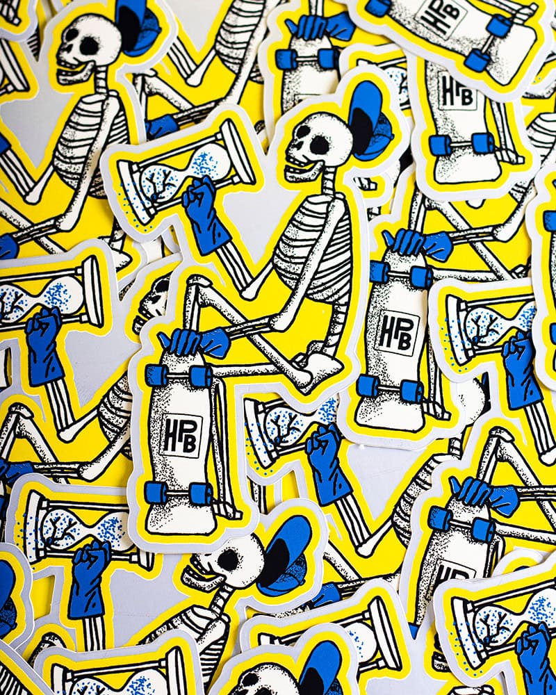 A pile of stickers featuring a cartoon skeleton in blue gloves and shoes, sitting on a yellow-outlined skateboard with “HPB” written on it. The skeleton has a blue hat and is smiling.