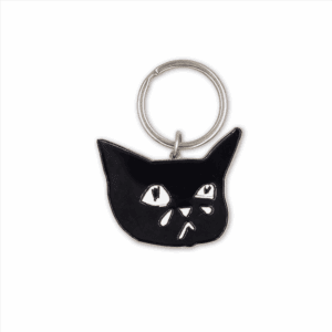 The Sad Cat Enamel Keychain features a black cat's face with wide, sad eyes and a tiny teardrop, attached to a simple silver keyring.