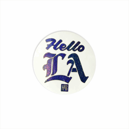 A round white Blue Hello LA Sticker (2 pack) featuring bold, glittery purple-blue "Hello LA" text in a decorative font, plus a small square "HPB" logo beneath the letters.