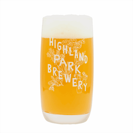 A glass of hazy golden beer with a foamy head is poured into the Native Plants Glass, featuring white floral illustrations and "Highland Park Brewery" printed on it, set against a plain white background.