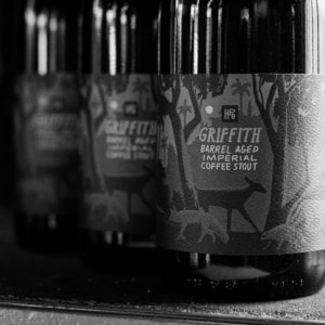 Black-and-white photo of bottles labeled “Griffith Barrel Aged Imperial Coffee Stout.” The label features silhouettes of trees and animals, lined up neatly—a perfect find for any beer membership collection.
