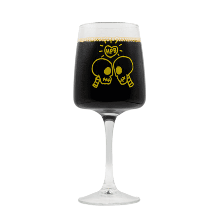 The Bottle Friends Brunch Glass 2026 features a yellow graphic of two cartoon skulls facing each other with "HPB" in a speech bubble, printed on the glass and pictured here filled with a dark liquid.