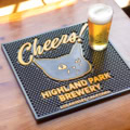 A glass of beer rests on the HPB Sad Cat Cheers! Bar Mat, which features a cartoon cat, "Cheers!", and "Highland Park Brewery, Los Angeles, California," all atop a wooden table.