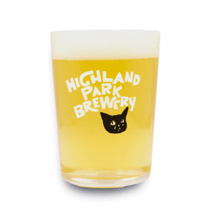 A glass of pale beer with foam on top, served in the Sad Cat Tumbler featuring the words “Highland Park Brewery” and a black cat face printed on the glass.